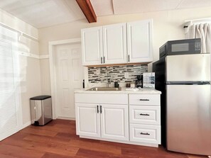 A compact kitchen with white cabinets, a stainless steel refrigerator, and a tiled backsplash. - Modern Studio Escape 10min to Legoland (Winter Haven)
