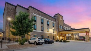 A hotel with a modern design, featuring a stone facade and a covered entrance. There are several cars parked in front, and the sky has a pink and purple hue, indicating sunset. - 2 Classic Suites Close to Loveland Sports Park + Pool and Breakfast Included (Johnstown)
