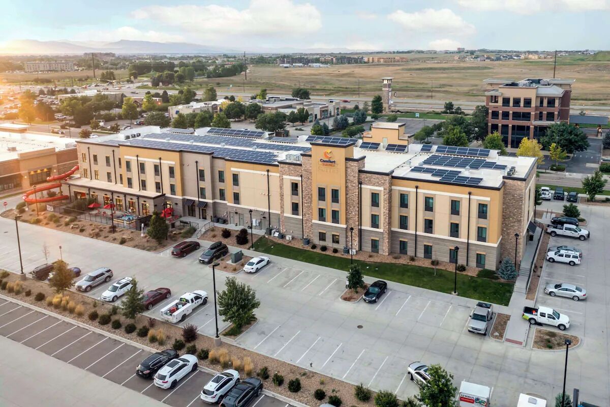 A hotel with a parking lot, solar panels on the roof, and a view of the surrounding area.