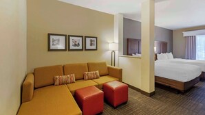 Una habitación de hotel con sofá, otomanas, cama y cuadros en la pared.