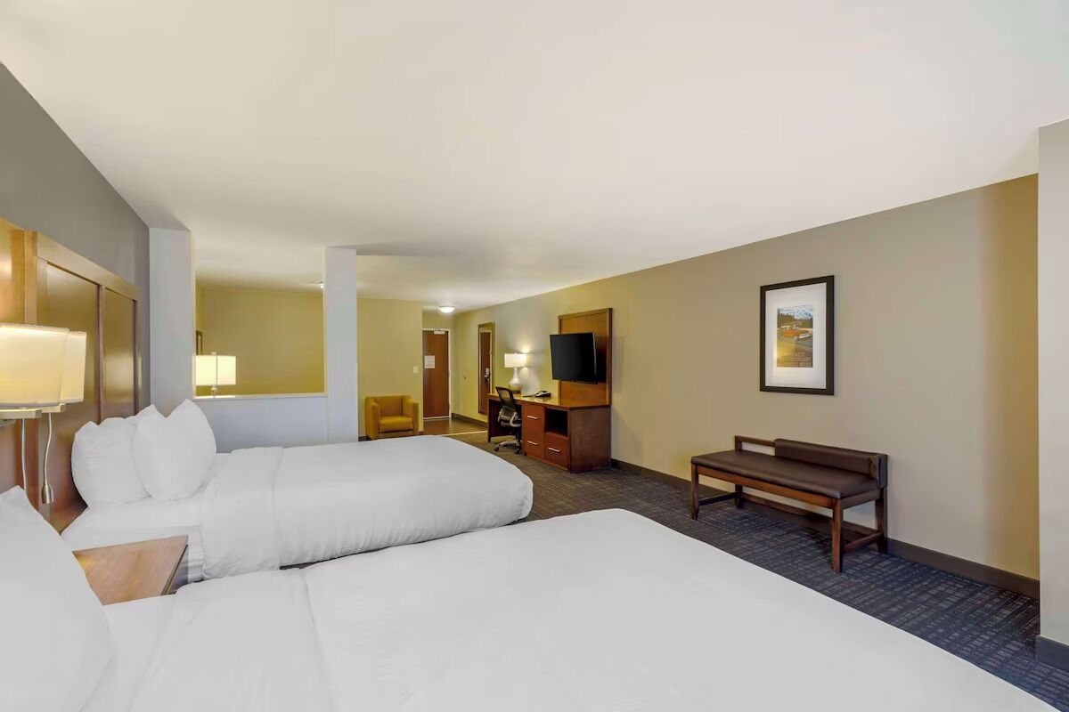 A hotel room with two beds, a desk, a chair, a TV, and a framed picture on the wall.