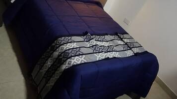 A bed with a blue bedspread and pillows, a patterned throw blanket, and a wall-mounted light fixture.