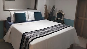 A neatly made bed with a patterned throw, a large mirror above it, and a decorative chair with a blue and white color scheme. -  Hotel Tierra y Mar Boutique (Cartagena)
