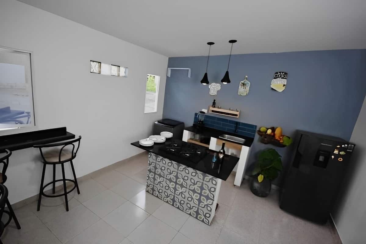A compact kitchen with a black countertop, two bar stools, a small island, and a refrigerator.