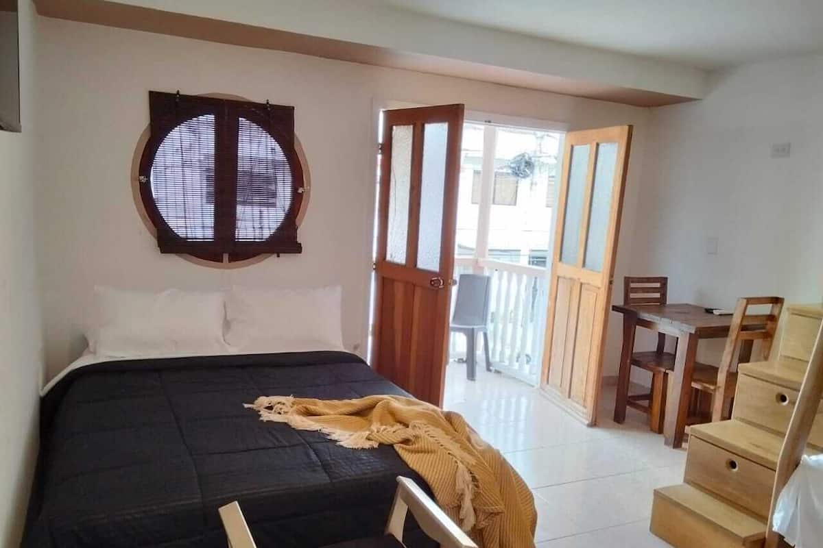 A bedroom with a bed, a wooden chair, a desk, and a window with blinds.
