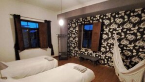 Ein Hotelzimmer mit zwei Betten, einem großen Fenster mit Vorhängen, einer Wand mit einem Blumenmuster und einem Hängestuhl.