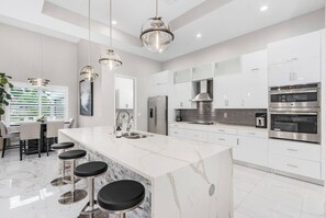 Una cocina moderna con armarios blancos, una isla de mármol, electrodomésticos de acero inoxidable e iluminación colgante.