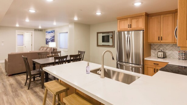 A modern kitchen with a central island, stainless steel appliances, wooden cabinets, and a dining area with a sofa and chairs. - Location, location!  Spacious 4-BR double apartment near Cottonwood Canyons (Cottonwood Heights)