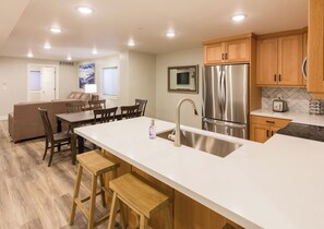 A modern kitchen with a central island, stainless steel appliances, wooden cabinets, and a dining area with a sofa and chairs.