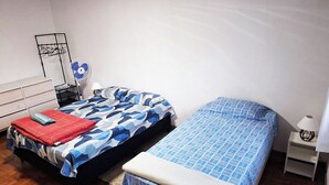 Una habitación con dos camas, un ventilador, una lámpara y una mesita.