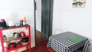 Una habitación pequeña con una mesa a cuadros, un estante rojo con utensilios de cocina y una puerta que da al exterior.