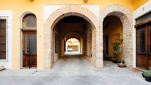 Un pasillo con tres arcos de ladrillo, suelo de baldosas y una puerta a la izquierda.