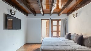 Un dormitorio con cama, televisor montado en la pared y techo de madera.