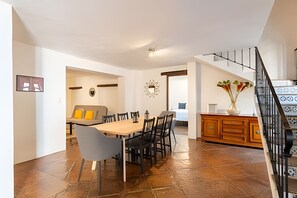 Un comedor amplio con una mesa y sillas de madera, un sofá con cojines amarillos, y una zona de cocina con armarios de madera y un florero con flores.