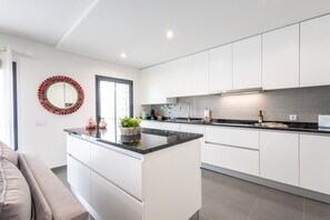 Una cocina moderna con armarios blancos, una isla central y un amplio ventanal.