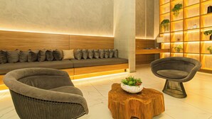 Een moderne lobby met een bank, twee fauteuils, een houten bijzettafeltje en een wand met potplanten.