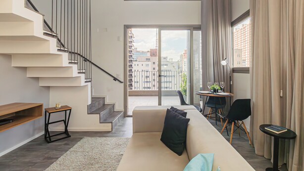 Een moderne woonkamer met een trap, een bank, een kleine tafel en een balkon met uitzicht op de stad.
