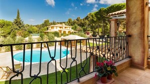 A balcony with a view of a swimming pool, a garden, and a distant building.