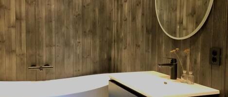 A modern bathroom with a freestanding bathtub, a vanity with a mirror, and wooden paneling on the walls.