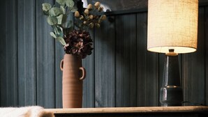 A dark wooden table with a lamp and a vase of flowers. - Sov Lodge (Vaga)