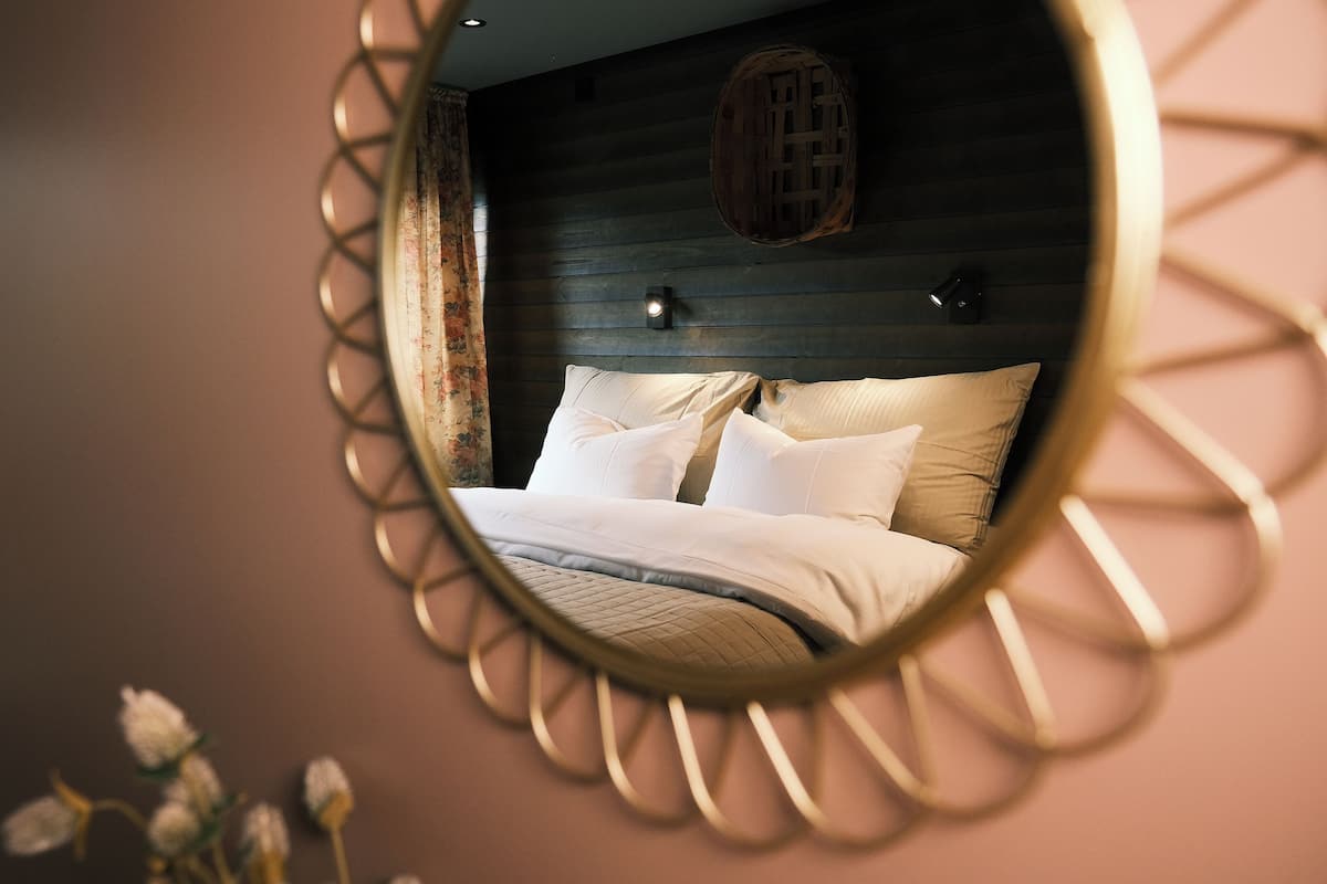 A bedroom with a bed, a headboard, a wall-mounted light, and a decorative mirror.