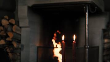 Dos velas frente a una chimenea con leña a la vista.