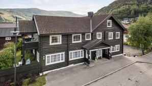 A two-story log cabin with a dark exterior and white trim, featuring a front porch and a garage. - Sov Lodge (Vaga)