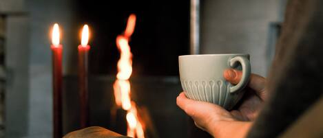 A hand holding a cup near a lit candle.