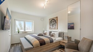A modern bedroom with a bed, bedside table, chair, and a large mirror. - 5 star apartment for 6 persons, ground floor with fenced garden (Zinnowitz)
