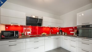 A modern kitchen with white cabinets, a red backsplash, and stainless steel appliances. - 5 star apartment for 6 persons, ground floor with fenced garden (Zinnowitz)