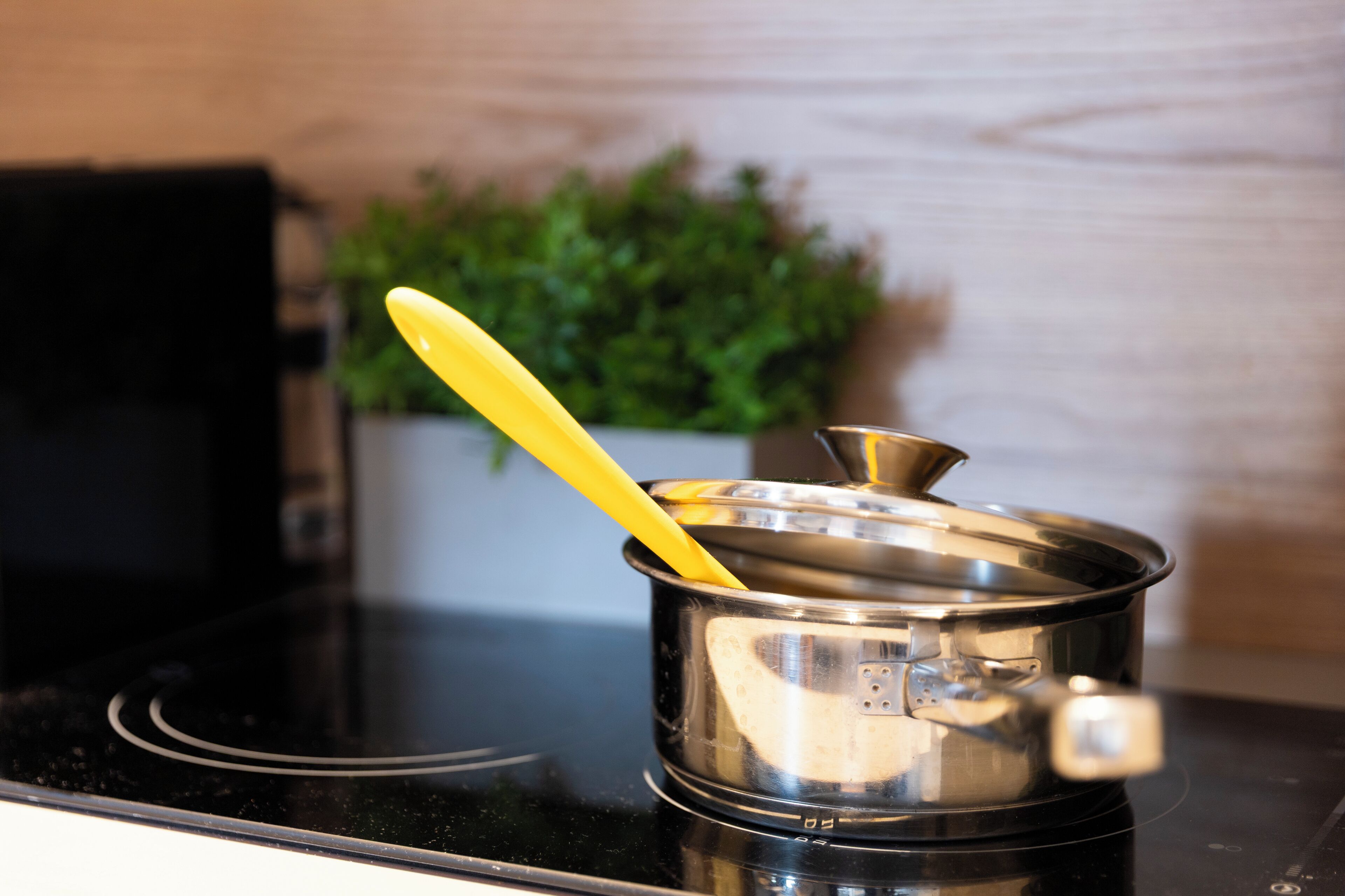 A stainless steel pot with a yellow handle on a black stovetop.