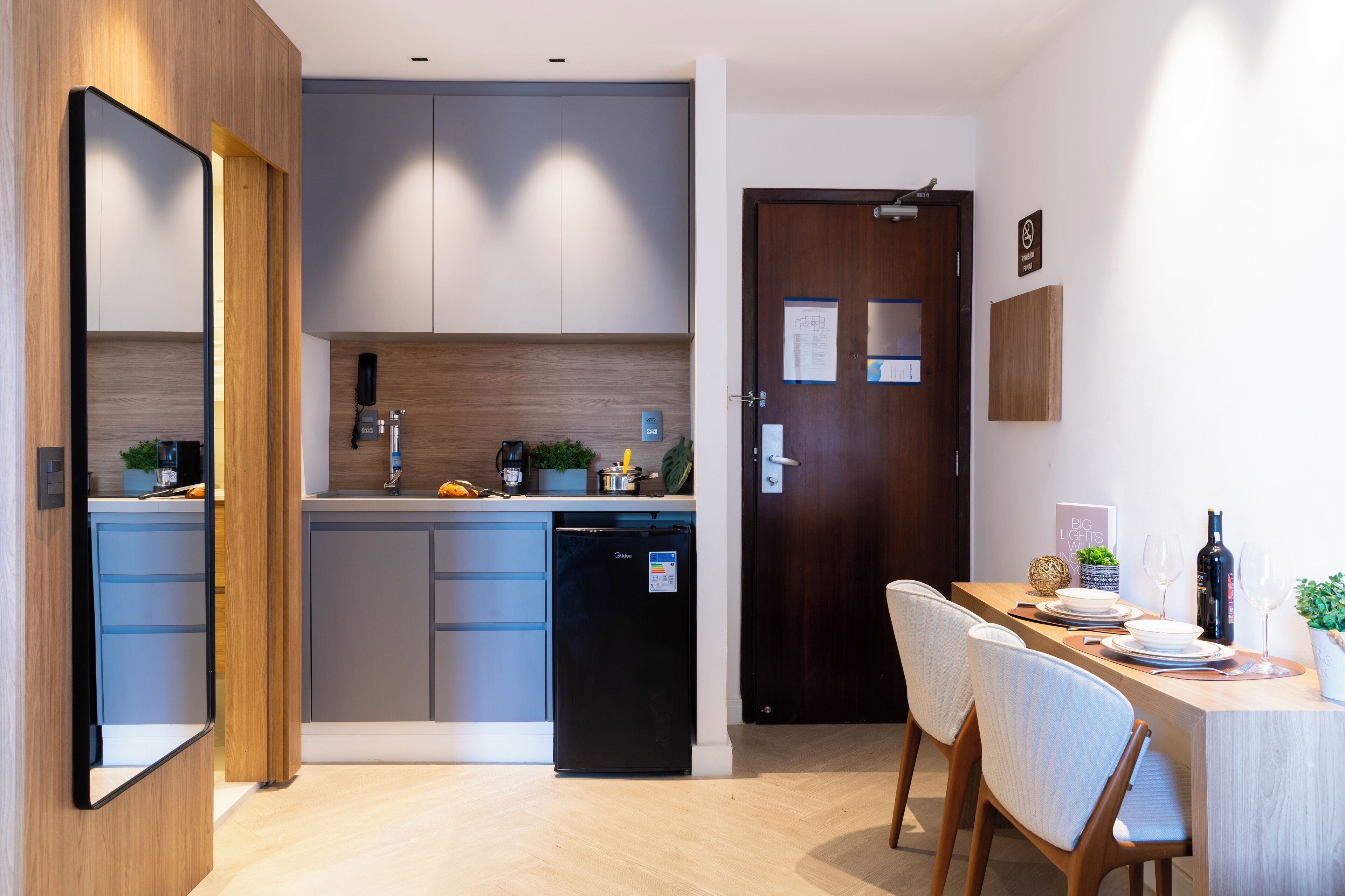 A modern kitchen with grey cabinets, a black refrigerator, and a wooden dining table with chairs.