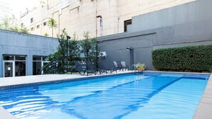 A rectangular swimming pool with clear blue water, surrounded by a tiled deck. There are lounge chairs and a potted plant near the pool. - Próximo a Paulista com piscina  (Sao Paulo)