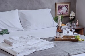 A neatly made bed with white linens, a bottle of Salton champagne, two glasses, and a tray with grapes. - 3 Quartos com vaga no Prado (Belo Horizonte)