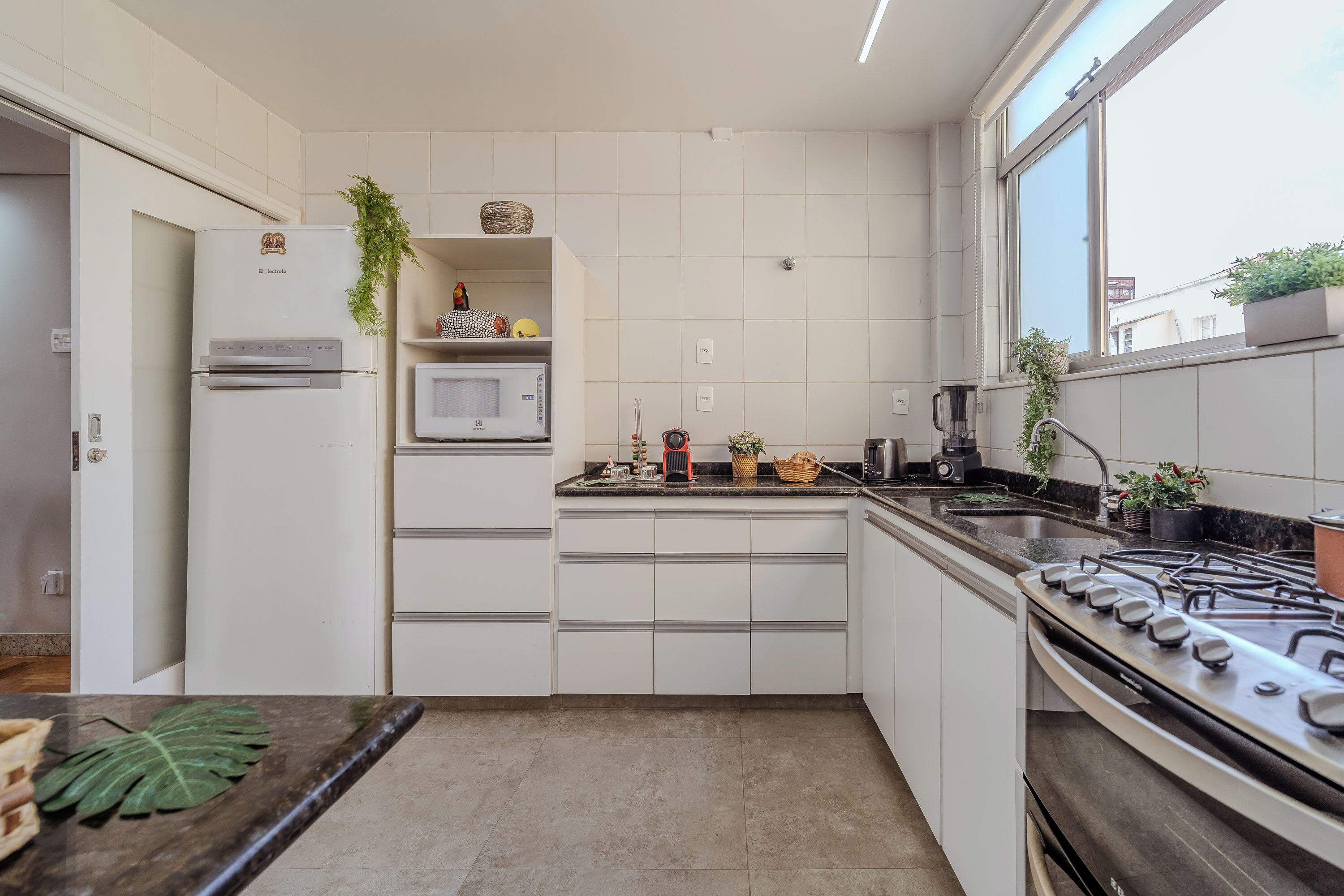 Una cocina moderna con armarios blancos, microondas integrado, estufa a gas y ventana con vistas a edificios.
