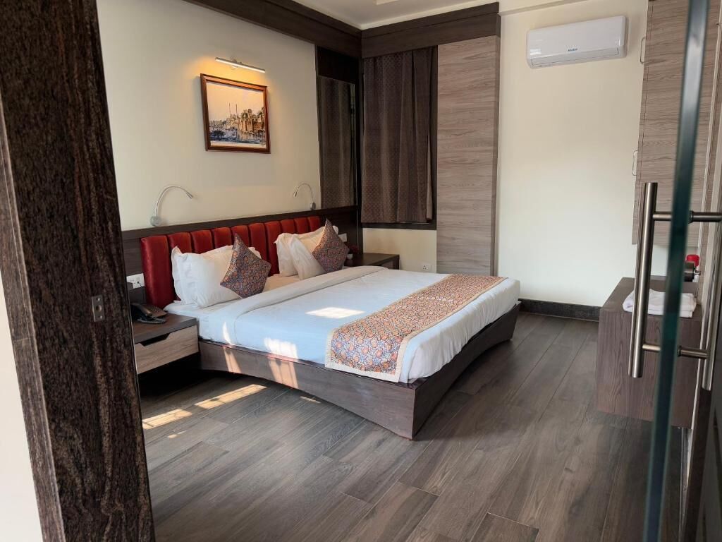 A modern hotel room with a large bed, a nightstand, a bedside table, a mirror, and a wardrobe.