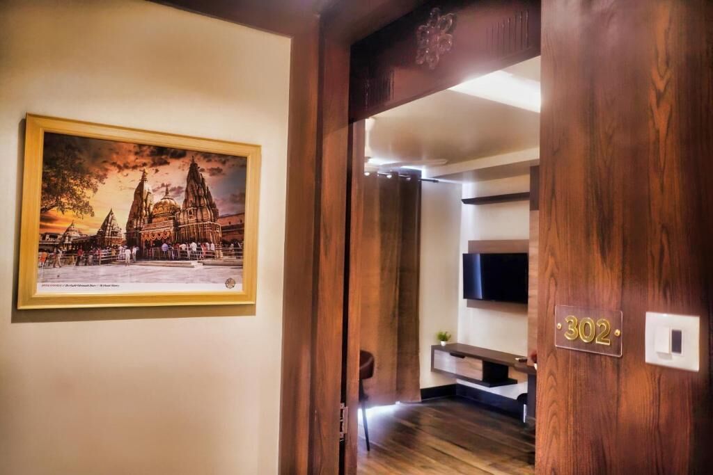 Ein Hotelzimmer mit Holztür, einem gerahmten Bild einer Kathedrale, der Zimmernummer '302' an der Wand und einem flachbildschirmfernseher, der über einer Holzkonsole angebracht ist.