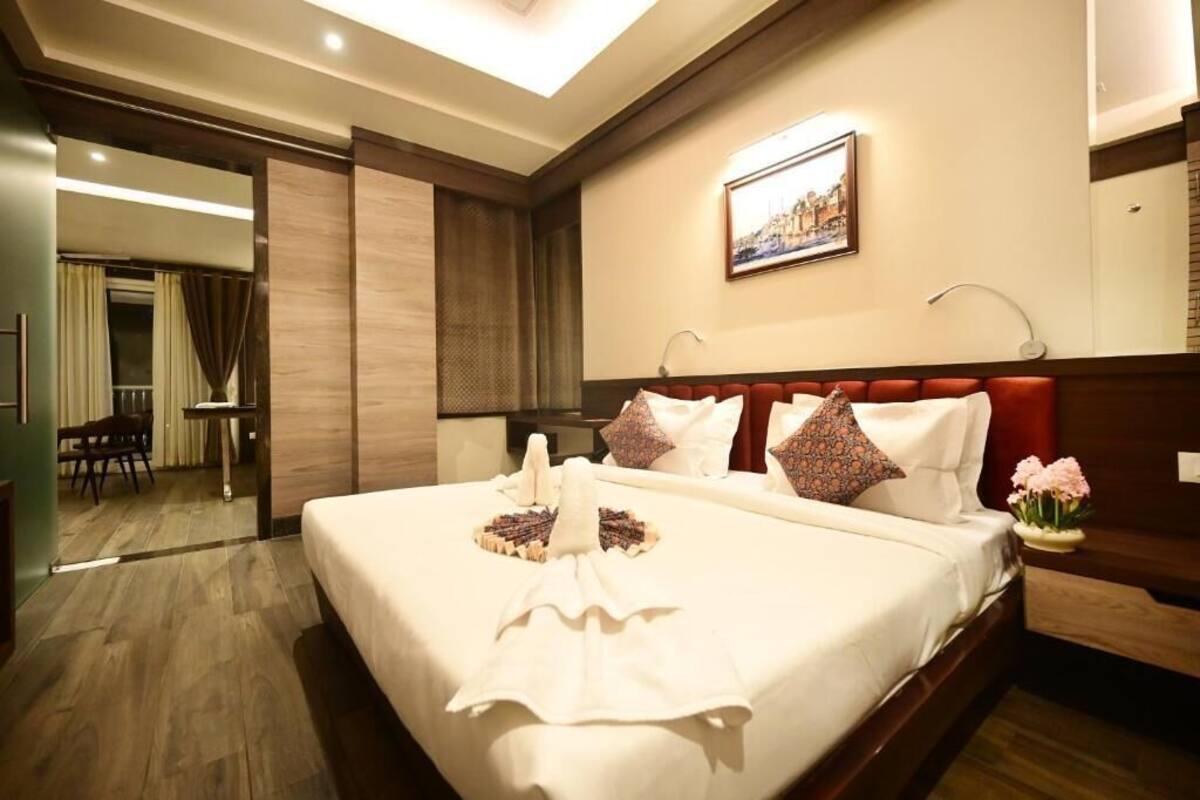 A hotel room with a large bed, a wooden headboard, a painting on the wall, and a small table with flowers.