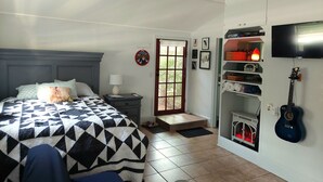 A bedroom with a bed, a ceiling fan, a TV, a guitar, and a fireplace. - Birds & Buns Bungalow (De Leon Springs)