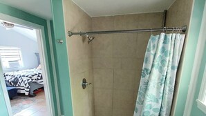 A bathroom with a shower, a toilet, and a sink. There is a door leading to another room. - Birds & Buns Bungalow (De Leon Springs)