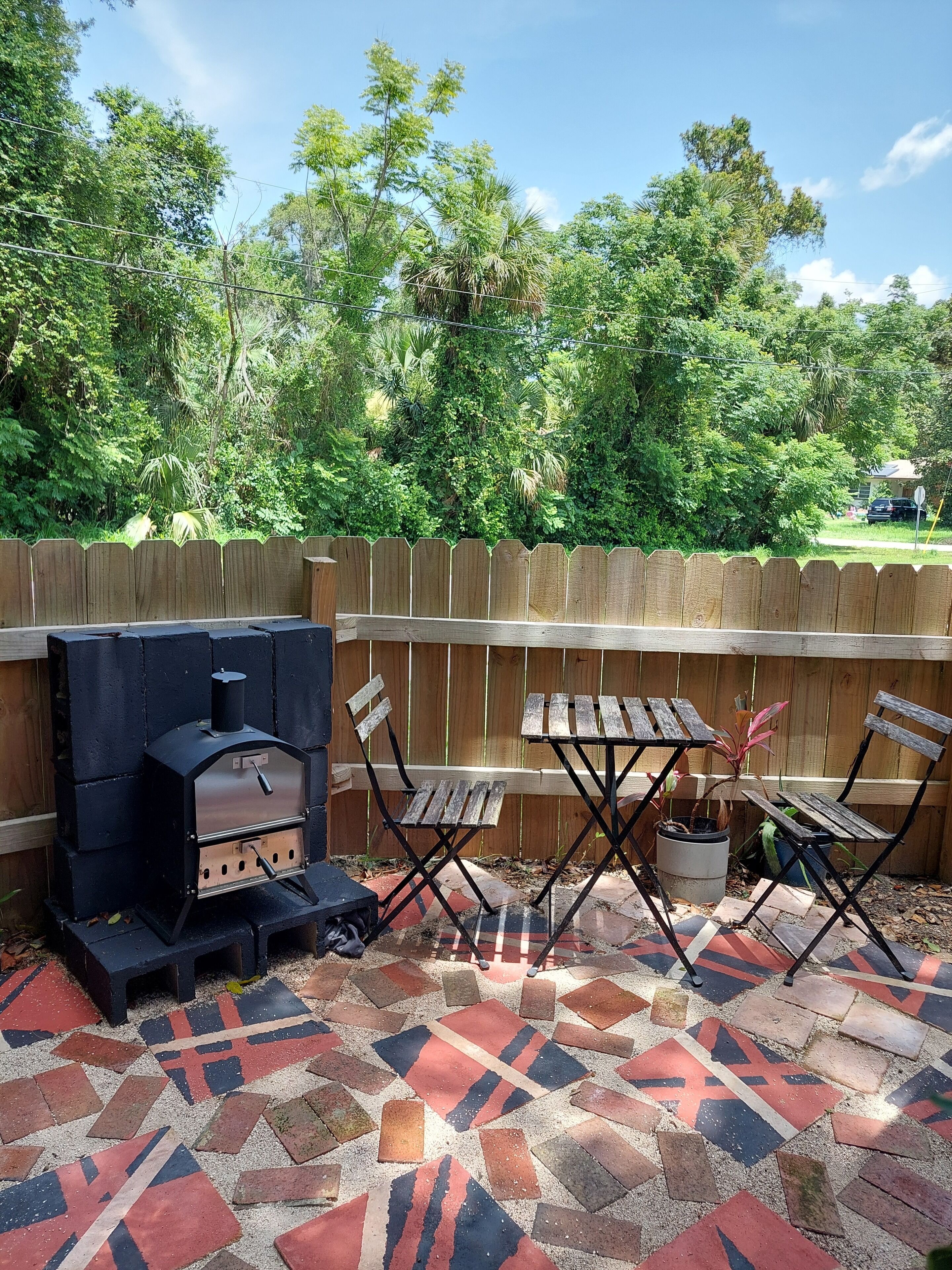 An outdoor patio with a barbecue grill, folding chairs, and a patterned tile floor.