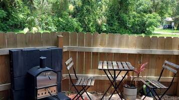 An outdoor patio with a barbecue grill, folding chairs, and a patterned tile floor.