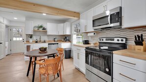 A modern kitchen with white cabinets, a stainless steel stove, and a wooden dining table with chairs.