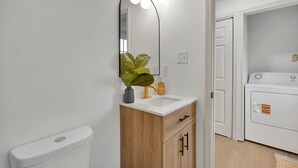 A bathroom with a white toilet, a wooden vanity with a mirror and lights, a sink, and a washing machine.
