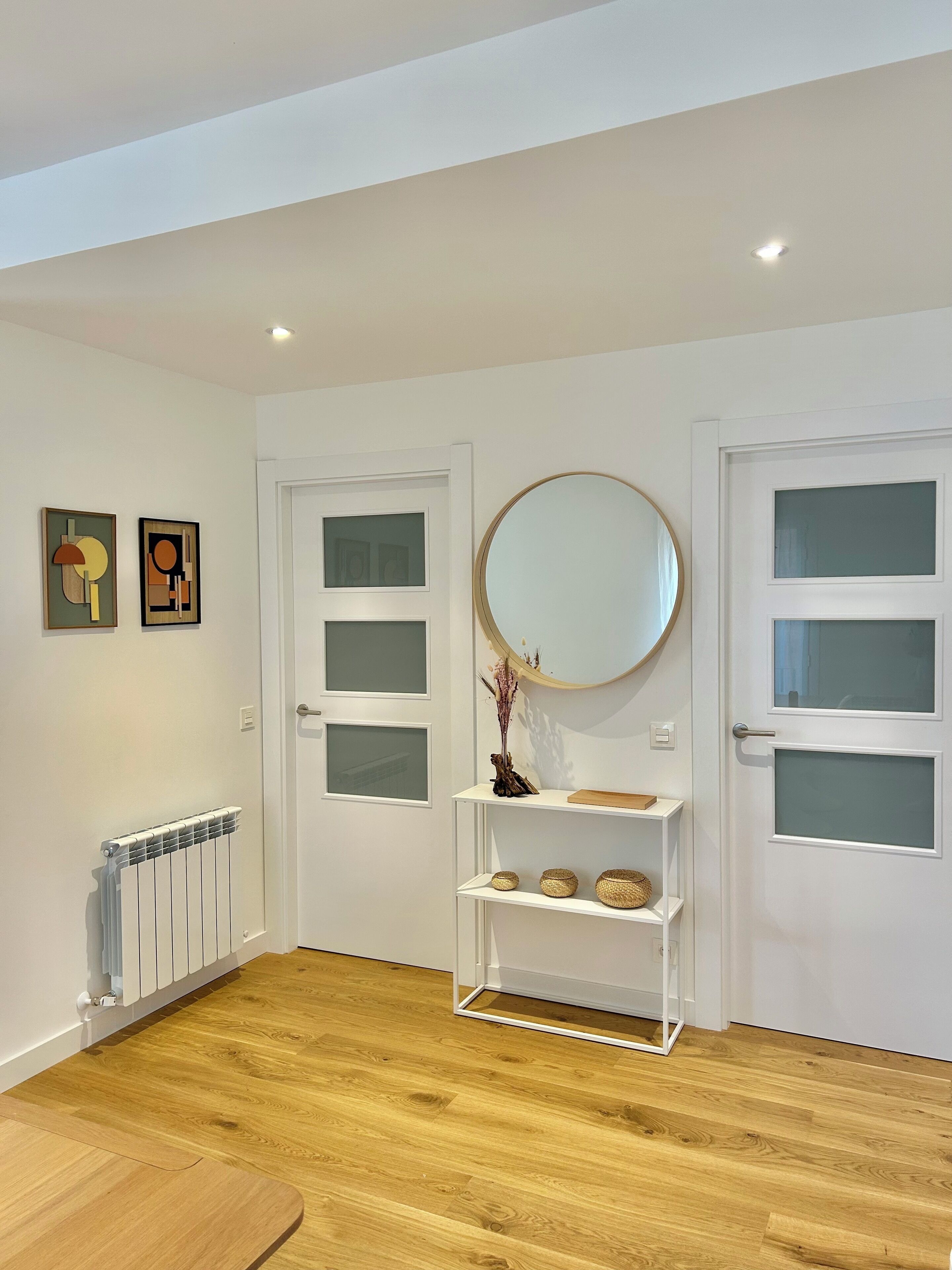 Un couloir avec des portes blanches, un radiateur et une étagère ornée d’objets décoratifs.