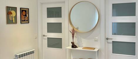 Un couloir avec des portes blanches, un radiateur et une étagère ornée d’objets décoratifs.