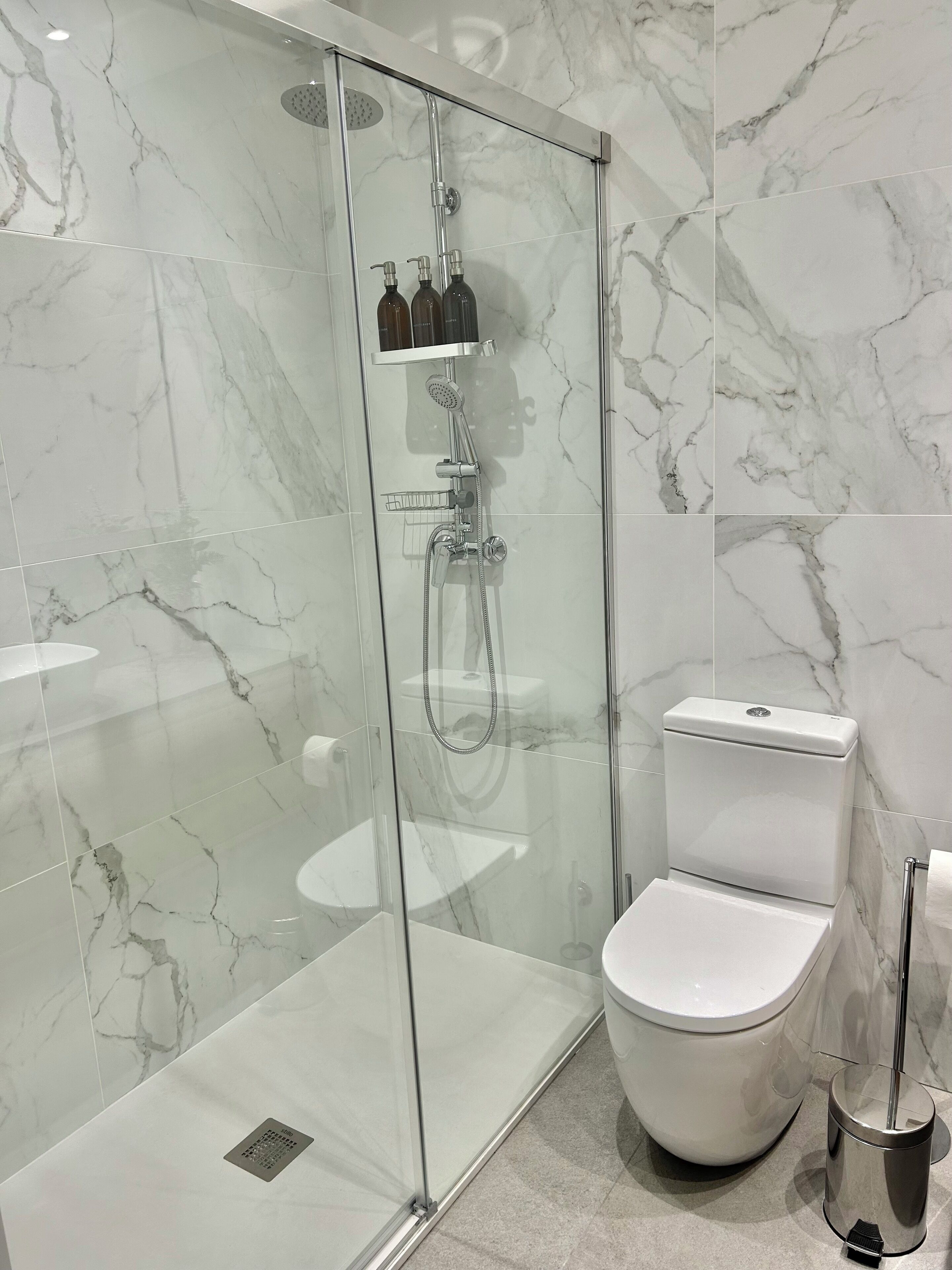 Ein modernes Badezimmer mit einer gläsernen Duschkabine, einer weißen Toilette und einer Handbrause.