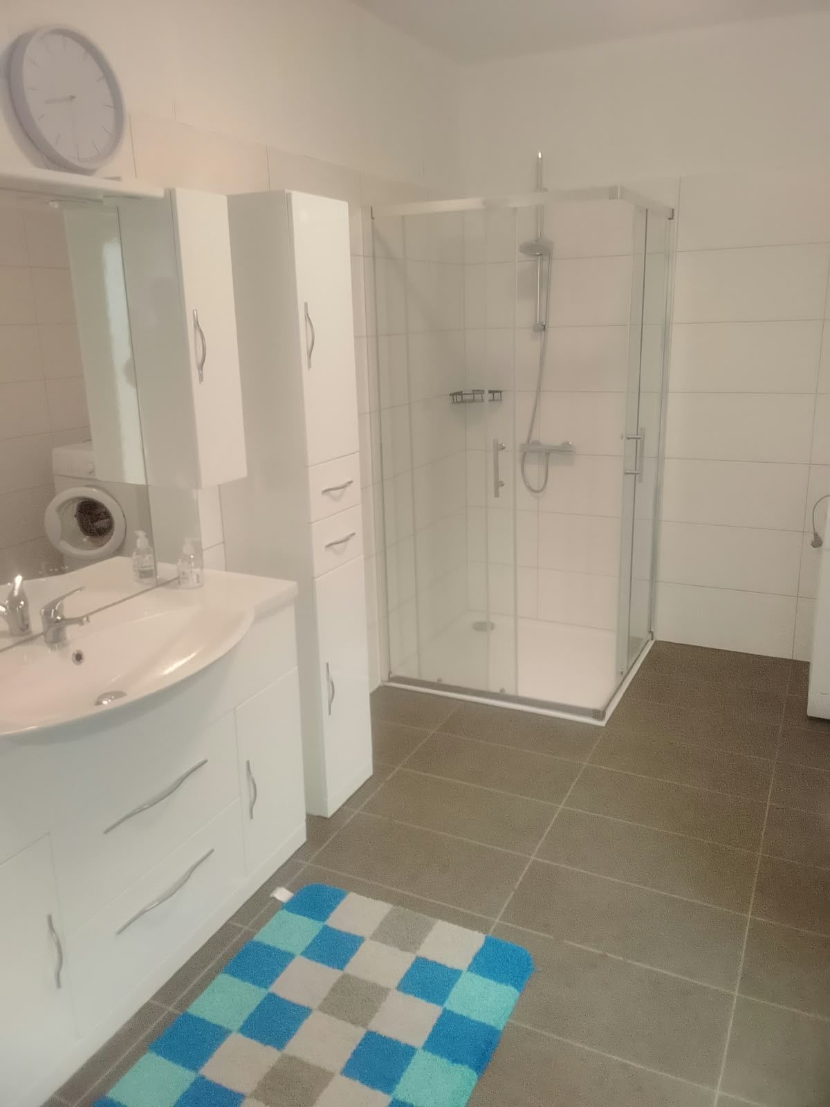 Une salle de bain équipée d’un lavabo, d’un miroir, de placards, d’une cabine de douche et d’un tapis à carreaux.