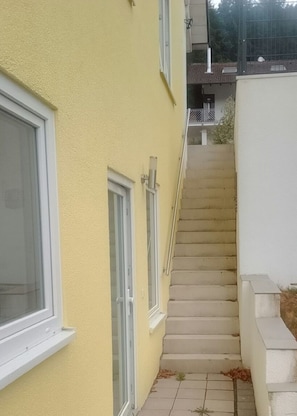 A residential building with a yellow exterior, a set of concrete stairs, and a white wall adjacent to the stairs. - Vacation apartment with a view of the Neckar (Eberbach)