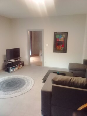 Un salon avec un téléviseur à écran plat, un canapé, une table basse et un tableau encadré au mur.